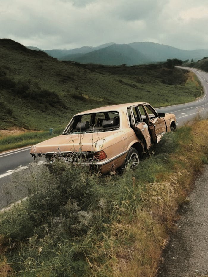 Old car left on roadside with scenic mountain backdrop.